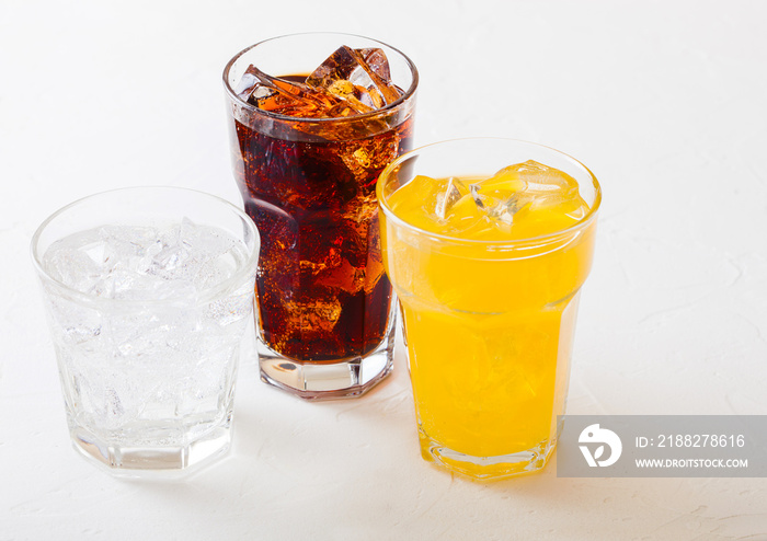 Glasses of soda drink with ice cubes and bubbles on stone kitchen table background. Cola and orange lemonade soda