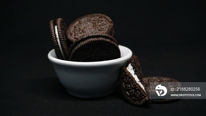 A bowl of Cookies isolated on black background. Chocolate cookies with white cream filling on white bowl