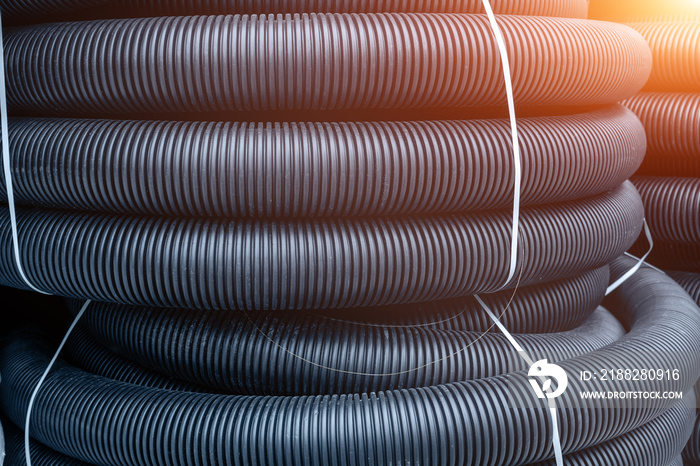 Many rolled colis of new black corrugated goffred plastic electric plumbing drainage pipe prepared for installation near building construction site. Drain sewage tube hose conduit pipeline