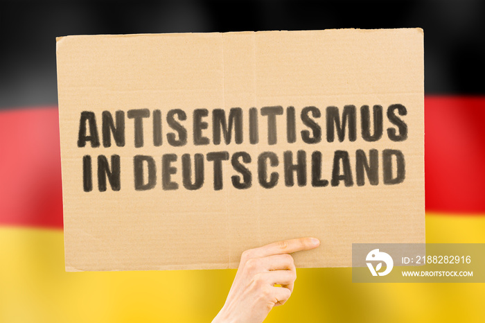 The phrase   Anti semitism in Germany   in German language on a banner in men’s hand with blurred background. Crime. Punishment. Conflict. Human rights