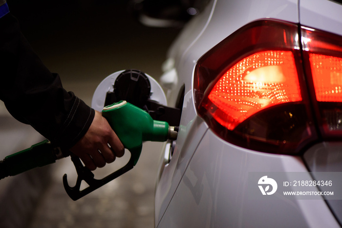 Gas station worker in workwear refueling luxury car with gasoline holding filling gun at the station.