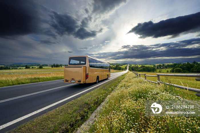 Bus traveling on the asphalt road in rural landscape at sunset with dramatic clouds