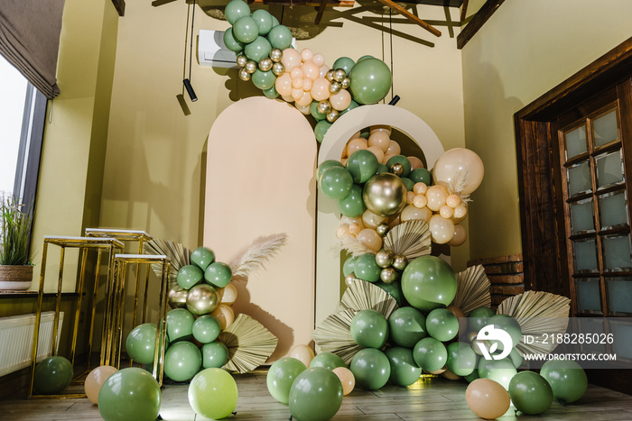 Arch decorated green, brown golden balloons, big paper decor leaves for wedding ceremony. Celebration baptism concept. Trendy autumn decor, photo wall. Copy space for text. Reception at birthday party