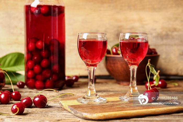 Glasses of sweet cherry wine on wooden background