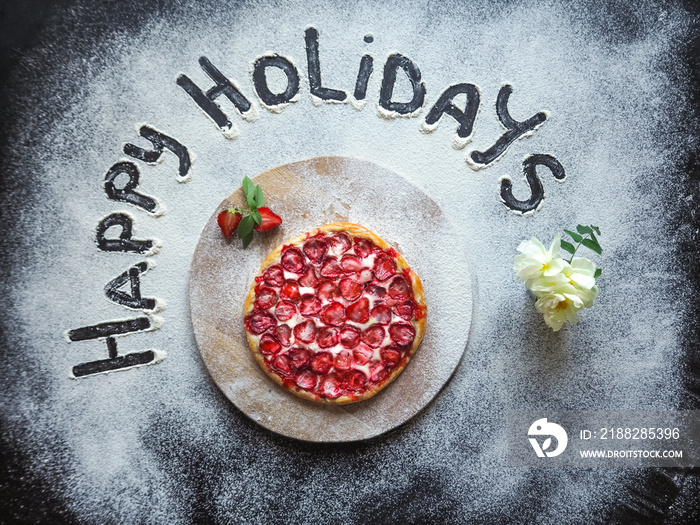 Pizza with strawberries and the words  happy holiday  made with flour on the black table.