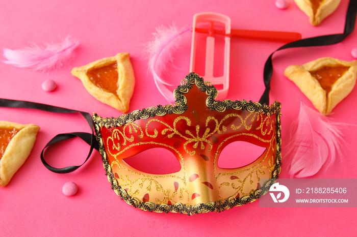 Carnival mask and Hamantaschen cookies with rattle for Purim holiday on color background