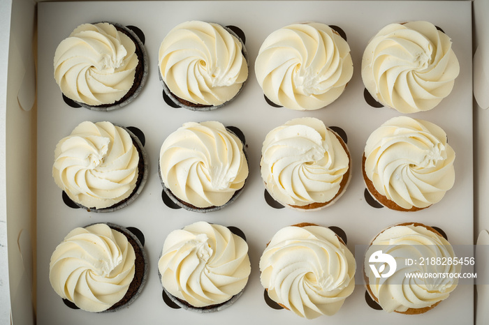 Set of brown chocolate and white vanilla cupcakes with whipped cream cheese tops in the white gift box. Flat lay