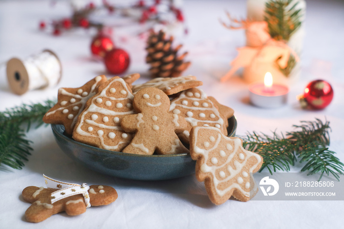 Various of Christmas cookies decorated with icing frosted in a bowl with festive holidays decoration atmosphere and candle light with green xmas tree branches