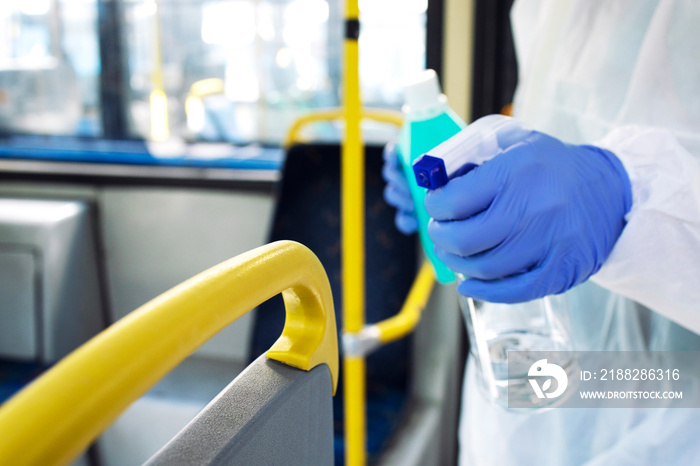 Unrecognizable cleaning person applying sanitizer or disinfectant on bus vehicle handlebars for public health. Stop spreading of virus.