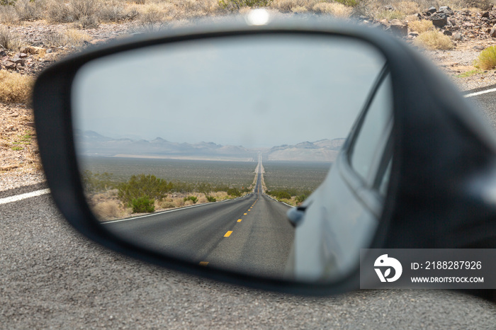 Looking into the rear view mirror of a car, at a long, straight road in Death Valley, California