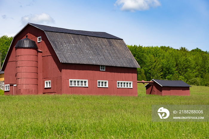 Large patrimonial barn with integrated grain silo painted in dark red in the Estrie region in late spring, Saint-Benoît-du-Lac, Quebec, Canada