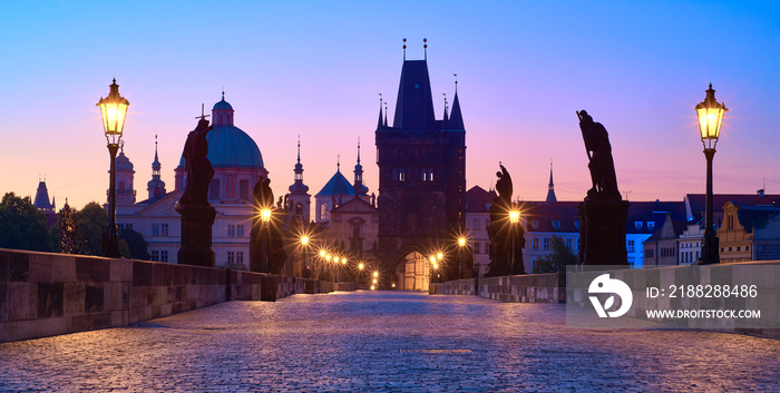 Charles Bridge at dawn, silhouette of Bridge Tower and saint sculptures with street lights in Prague, Czech Republic