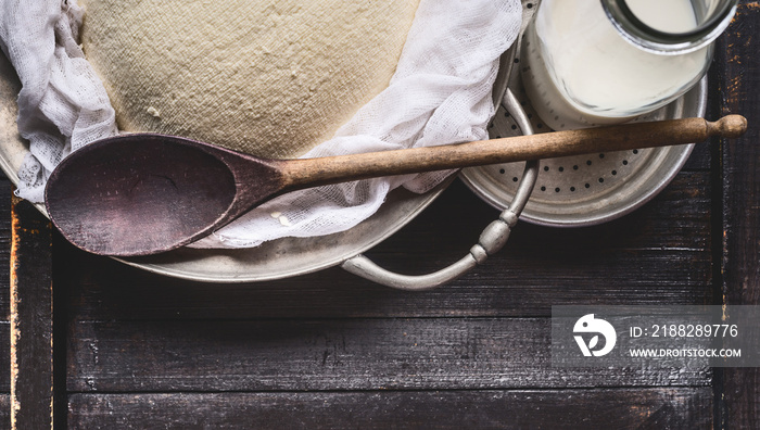 Fresh cheese making with cheesecloth , bottle of milk and wooden spoon on rustic background, top view, close up