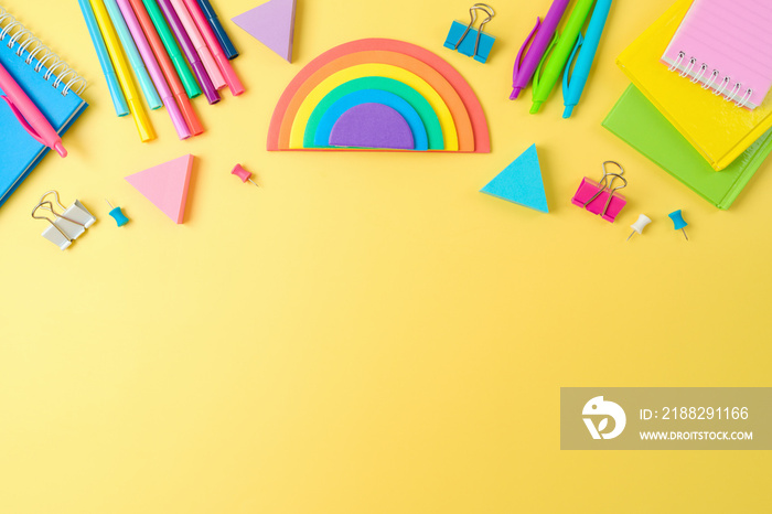 Back to school concept with notebooks, pens and rainbow sticky notes on yellow background. Top view, flat lay