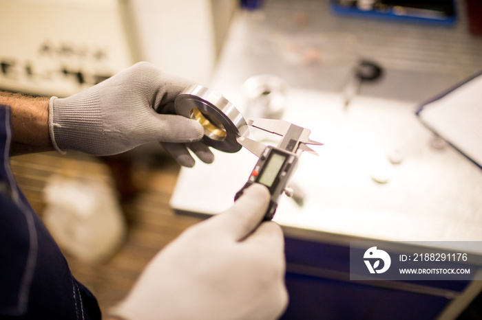 Engineer in gloves measuring width of steel detail with calipers during work in factory