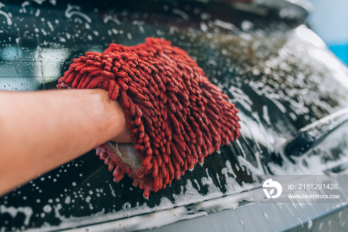 Car wash and detailing - the man holds the microfiber in hand and polishes or washing the car. Man cleaning automobile with sponge at car wash