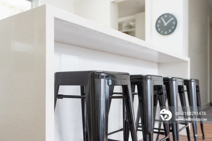 Closeup of black metal stools against white kitchen bench with clock in background (selective focus)