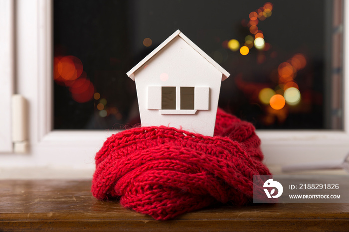 house in winter - heating system concept and cold snowy weather with model of a house wearing a knitted cap