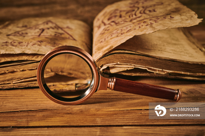 Magnifying glass and the ancient magic book on wooden table