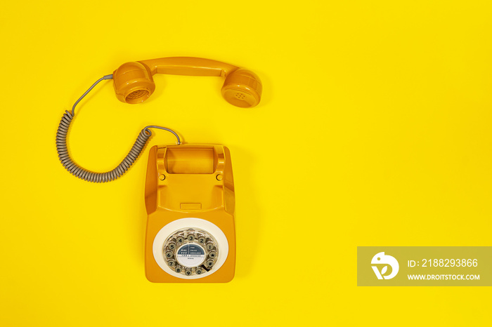 Yellow handset of a telephone on a yellow background.