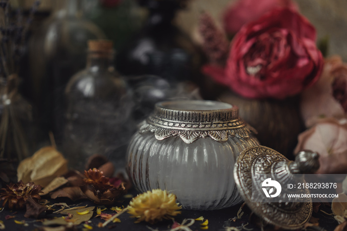 vintage jars, bottles, containers, flowers in smoke and dry leaves on a wooden table with warm light