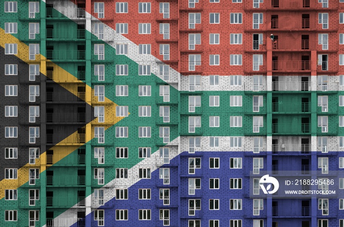 South Africa flag depicted in paint colors on multi-storey residental building under construction. Textured banner on brick wall background