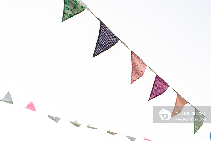 Pennants with blue sky background and pale colors hanging on a rope crossing the image during an outdoor event, space for text.