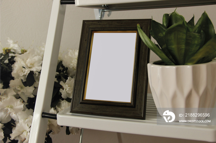 Blank wooden photo frame surrounded by home plants. Comfy details in the bedroom.