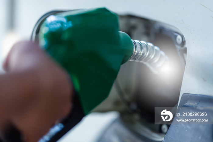 Man Handle pumping gasoline fuel nozzle to refuel. Vehicle fueling facility at petrol station. White car at gas station being filled with fuel. Transportation and ownership concept.