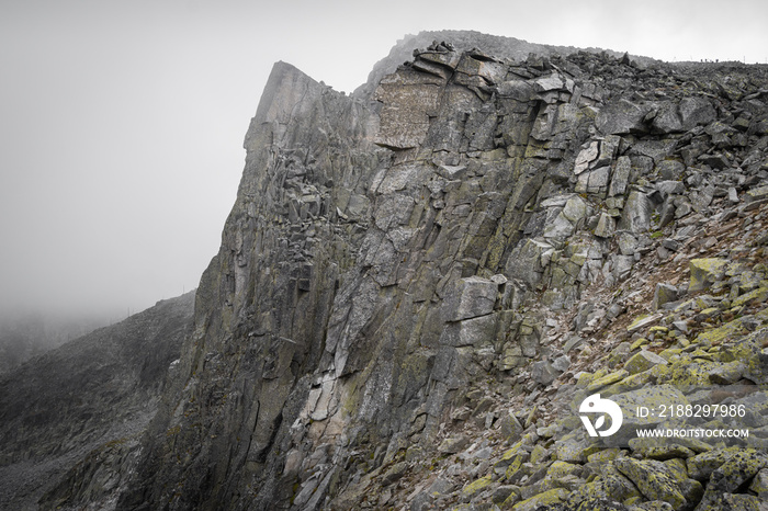 Impressive vertical cliff in front of Musala summit on Rila mountain in the fog and mountain hikers in the distance