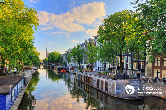 Houseboats at the UNESCO world heritage Prinsengracht canal with the Westerkerk (Western church) on a summer morning with a blue sky and clouds and a mirror reflection in Amsterdam, The Netherlands