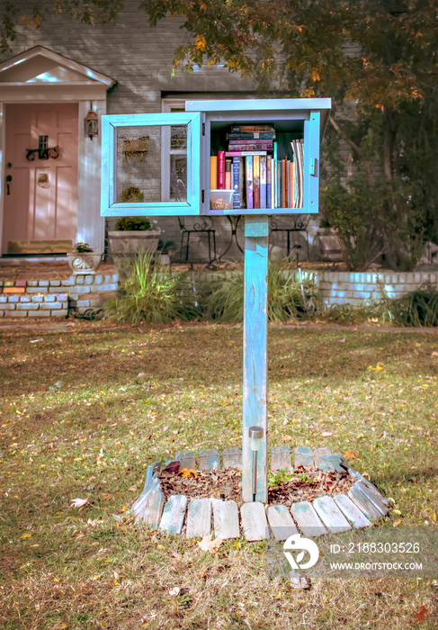 Homemade book box library in font yard of residential house open and full of books with a plastic co