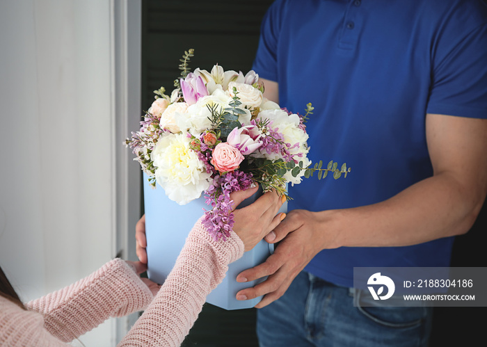 Young woman receiving beautiful flowers from delivery man at home