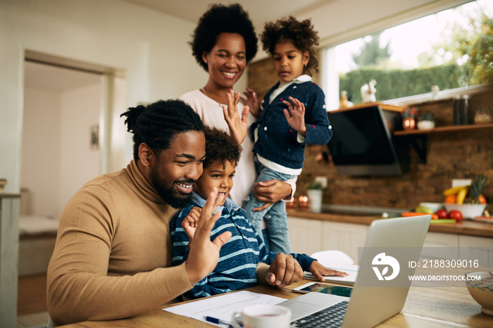 Happy African American family waving during a video call over laptop at home.