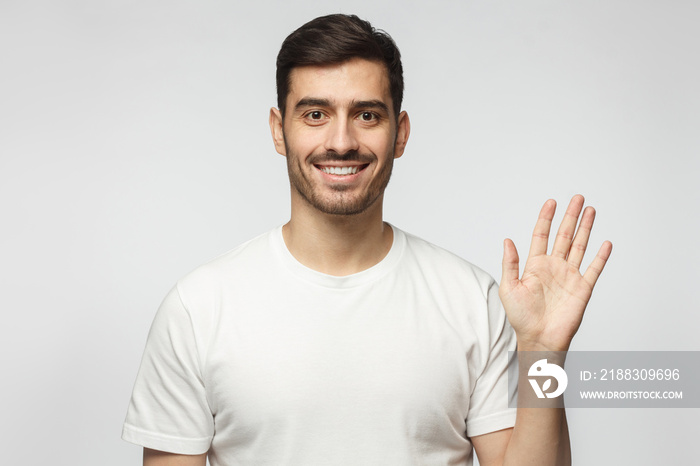 European man greeting someone with open hand, smiling, enjoying communication, isolated on gray back