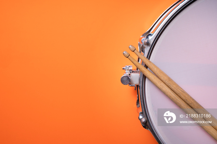 Drum stick and drum on orange table background, top view, music concept