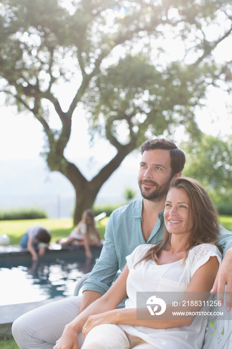 Happy couple relaxing on bench at sunny poolside