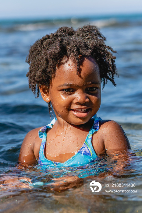 Retrato vertical de una pequeña niña muy sonriente de cabello afro mojada en la playa en un hermoso 