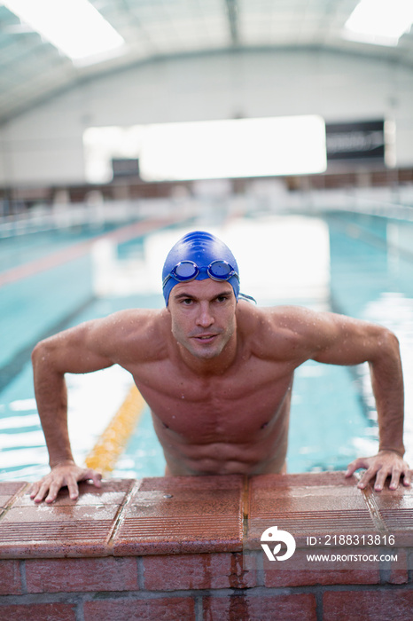 Portrait confident athletic male swimmer at edge of swimming pool