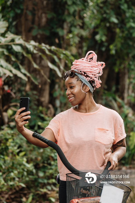 Imagen vertical de una hermosa mujer afroamericana con cabello rosado al aire libre tomándose un sel