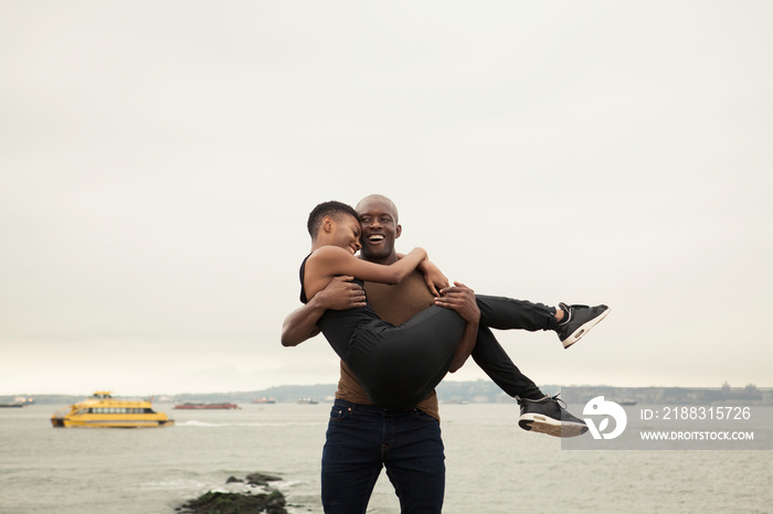 Happy boyfriend carrying girlfriend while standing by river against cloudy sky