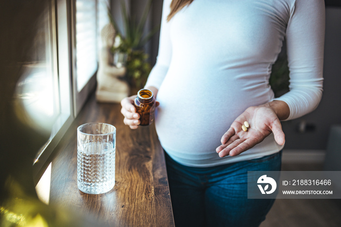 孕妇正在服用维生素药丸。孕妇手拿一杯水和维生素的特写