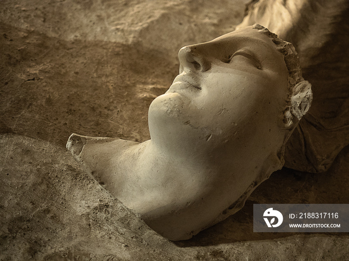 A broken statue head laying on the ground in Rome