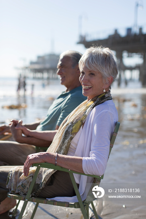 Happy senior couple relaxing in lawn chairs on sunny beach