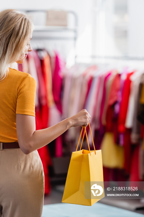 微笑的女人看着服装精品店的黄色购物袋