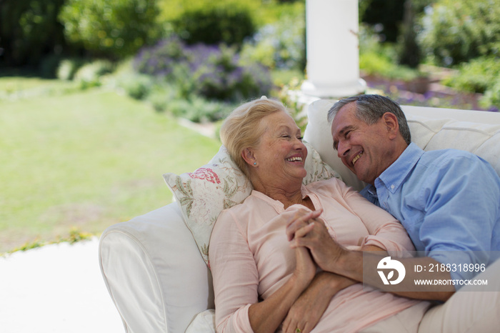 Happy senior couple holding hands and cuddling on patio sofa