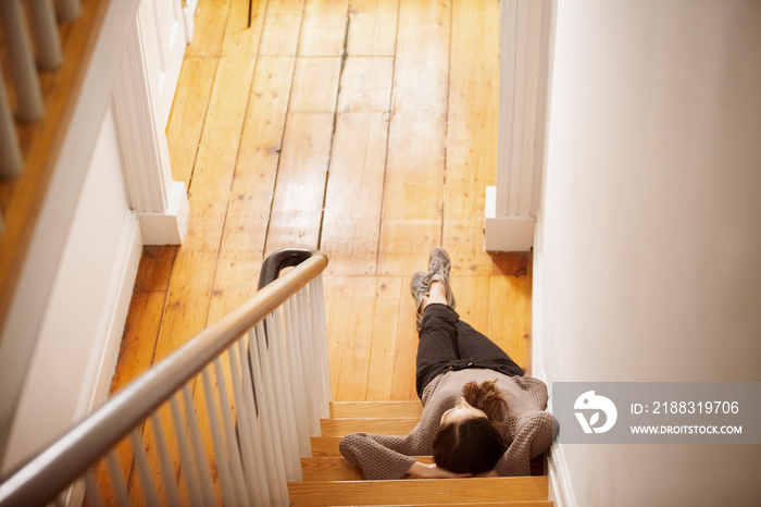 High angle view of woman with hands behind head sitting on steps at home