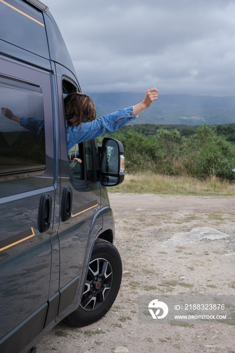 一个女人从一辆面包车的窗户望着风景。垂直照片。