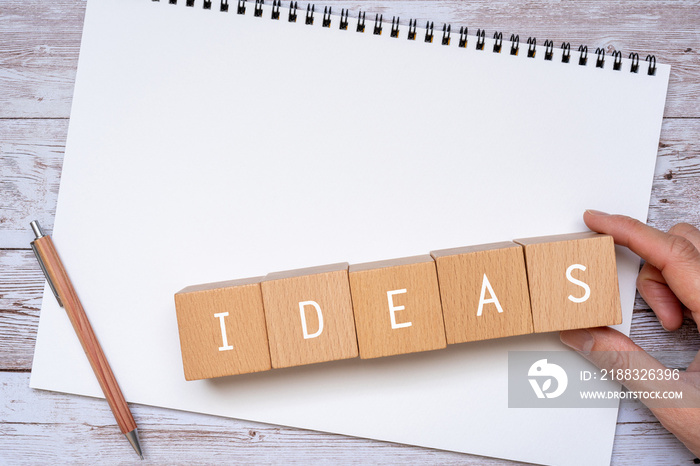 「IDEAS」と書かれた積み木、ノート、ペン、人の手