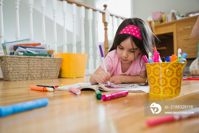 Little girl coloring in book while lying on floor